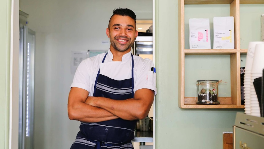 Ross, wearing a chef's uniform, stands in the hallway of a cafe.