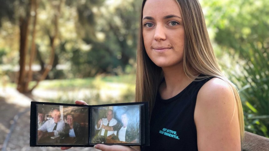 A woman seated on a bench holding two photos of her grandparents