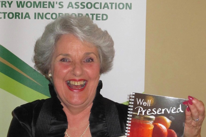 An older woman beaming while holding up a cook book.