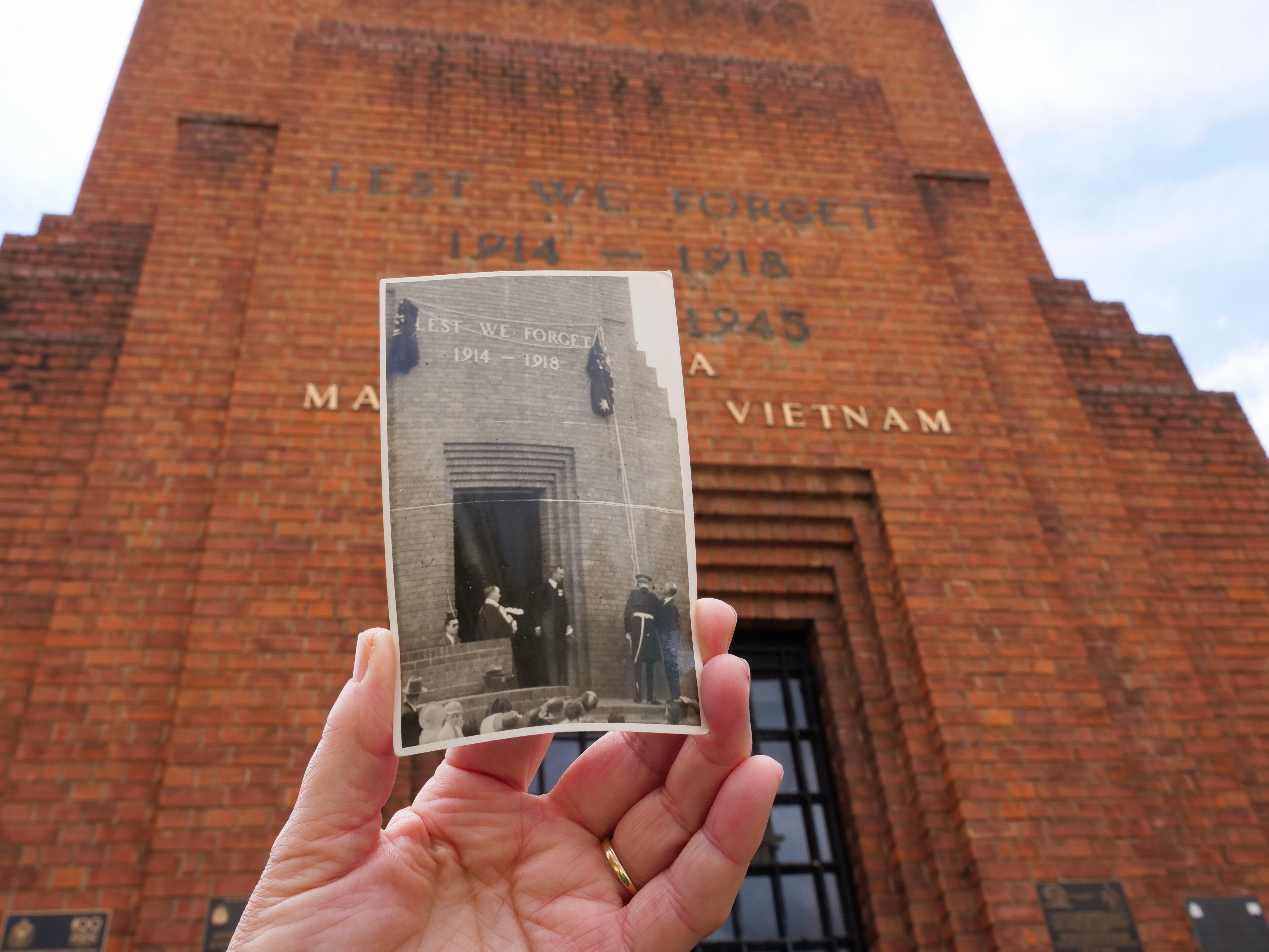 A black and white picture of people in front of a brick building being held up in front of the same building.