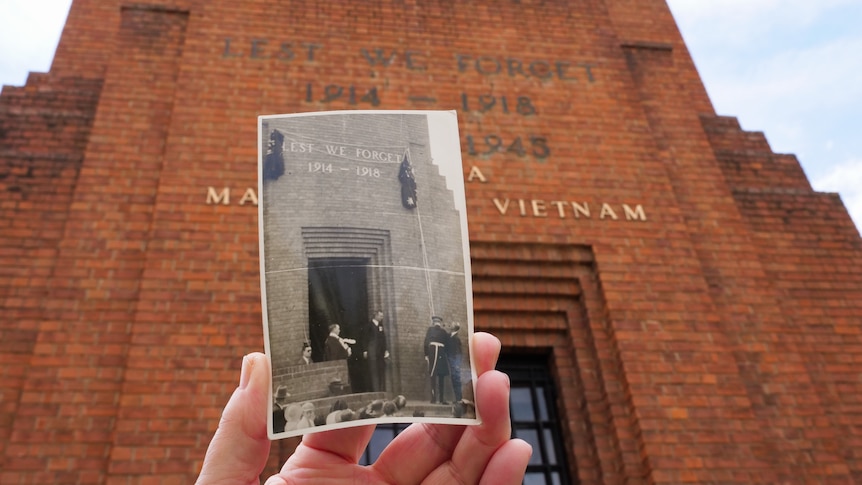 A black and white picture of people in front of a brick building being held up in front of the same building.