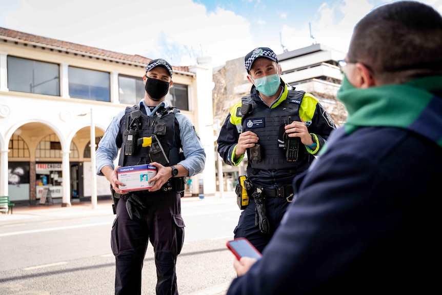 Two ACT policemen hand out facemasks in the Canberra CBD. Both are smiling