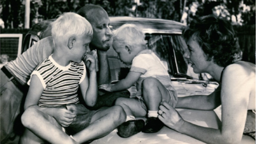 Black and white photo of a family in 1957, two boys mum and dad, boys sit atop a car 