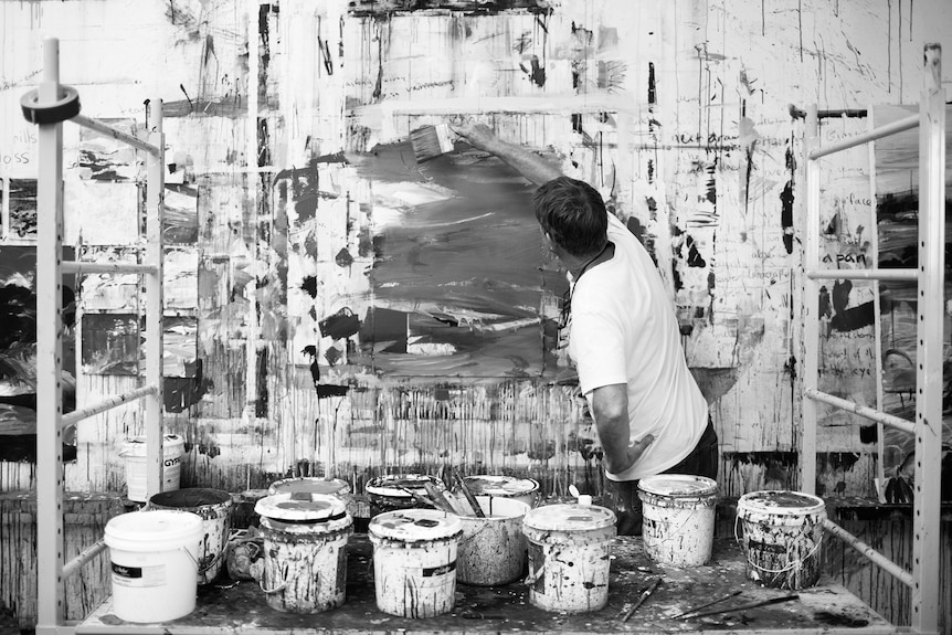 Man paints on a wall with buckets of paint in the foreground.