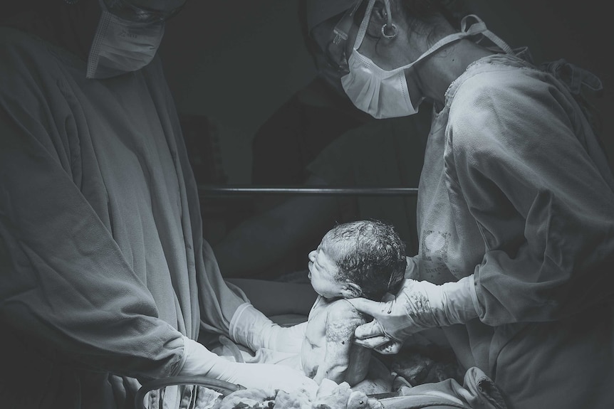 A surgeon holding a newborn baby.