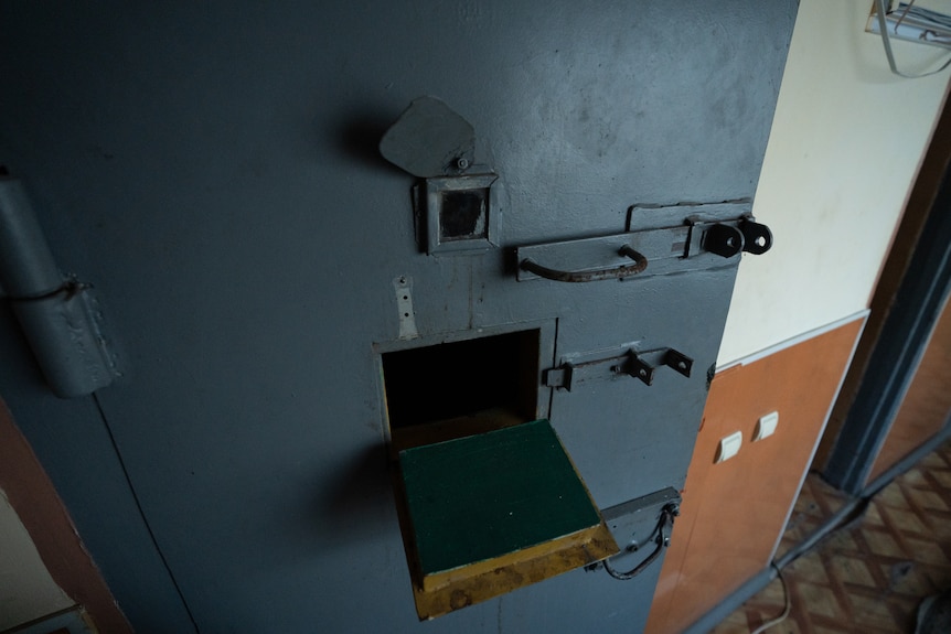 A blue door with a small opening and locks in a Ukrainian police station.