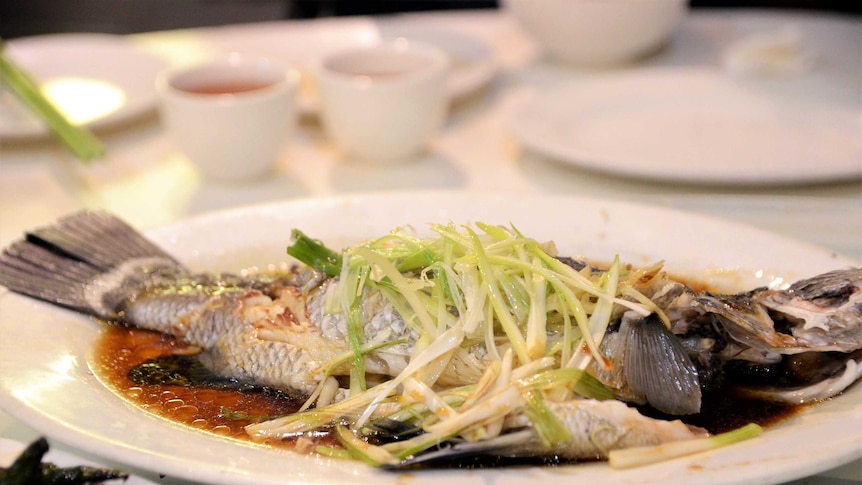 A full steamed fish dressed in spring onion and brown sauce.