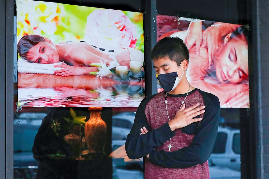 A man of Asian descent with his eyes closed lays his hand on his chest outside a massage parlour