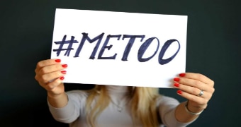 A woman holding a sign in front of her face that says #METOO.