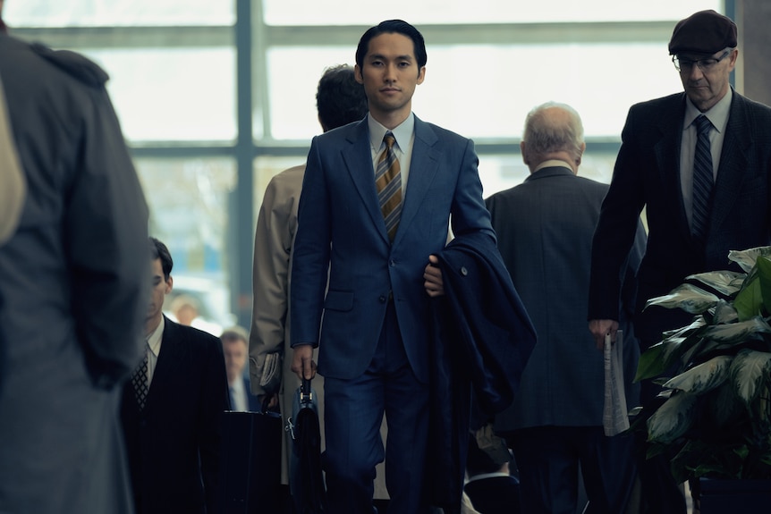 A young Korean man in a smart blue suit strides through a crowded airport.