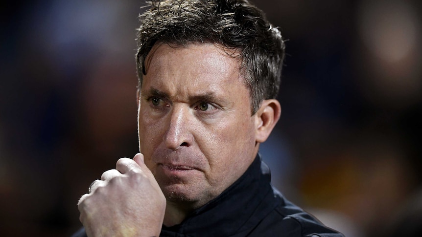 Robbie Fowler holds his clenched fist close to his mouth and looks stern