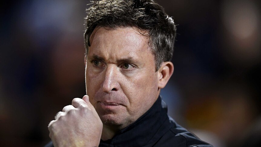 Robbie Fowler holds his clenched fist close to his mouth and looks stern