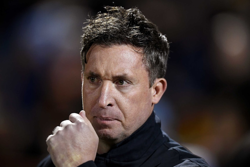 Robbie Fowler holds his clenched fist close to his mouth and looks stern