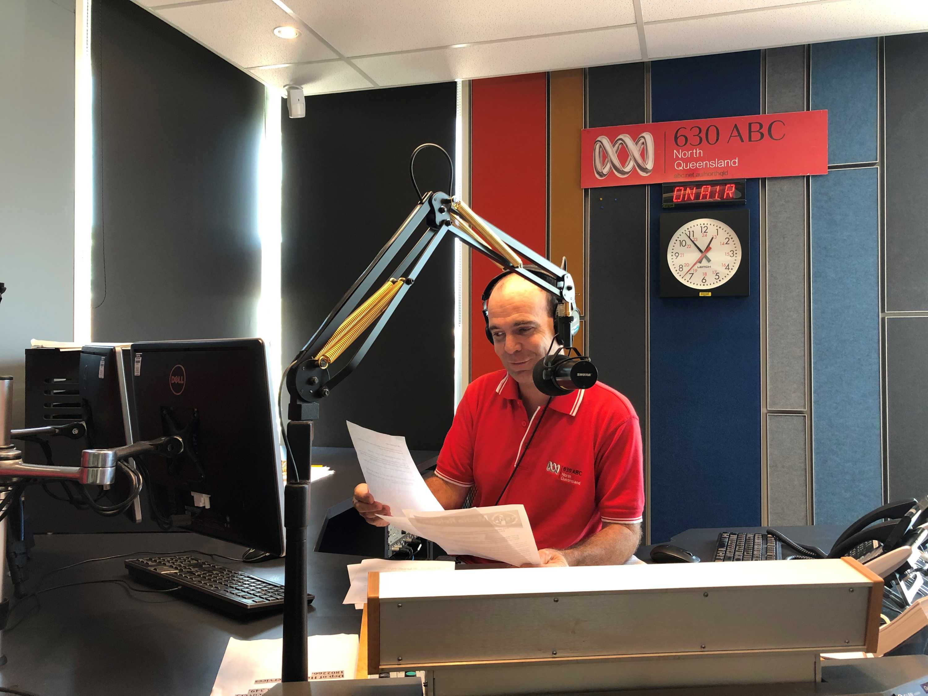 Hession in studio talking into microphone while holding sheets of paper.