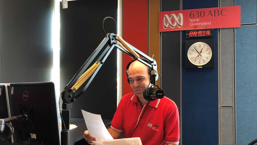 Hession in studio talking into microphone while holding sheets of paper.