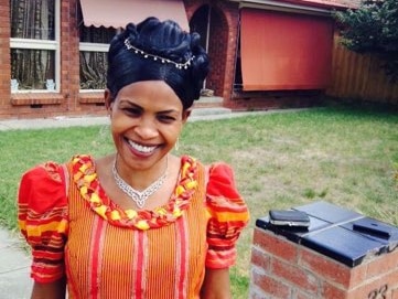 A woman in a dress standing at the front of a house.