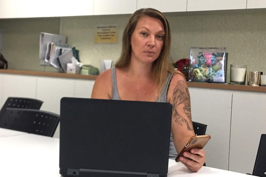 A woman sitting behind a laptop computer and holding a mobile phone