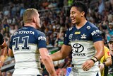 Two North Queensland Cowboys NRL players celebrate a try with a Wests Tigers opponent in the background.