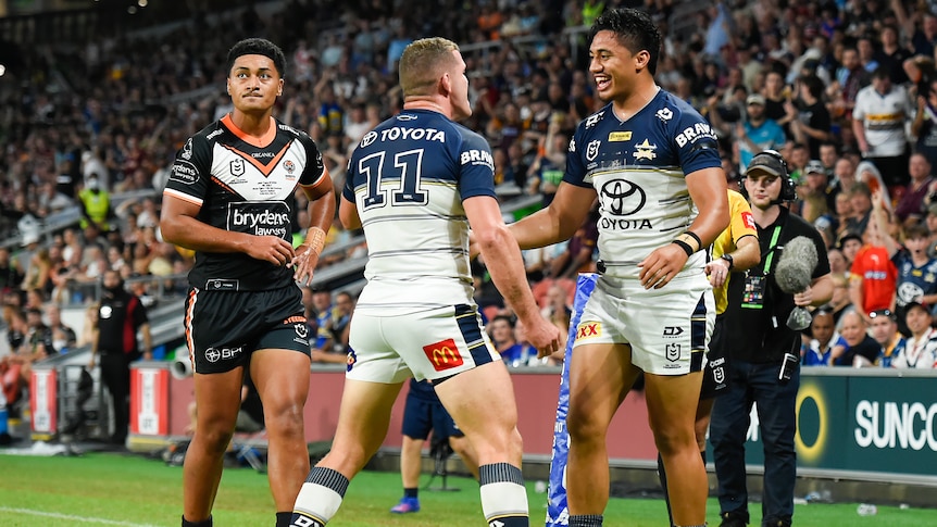 Two North Queensland Cowboys NRL players celebrate a try with a Wests Tigers opponent in the background.