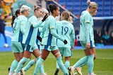 matildas soccer players on the field in their aqua coloured jersey and shorts celebrating a goal