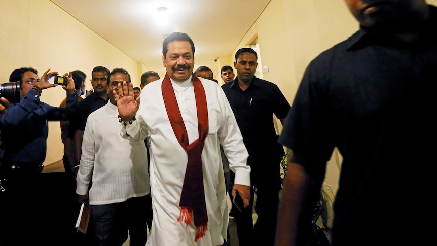 Sri Lanka's disputed Prime Minister Mahinda Rajapaksa walks down a corridor of parliament surrounded by a media throng.