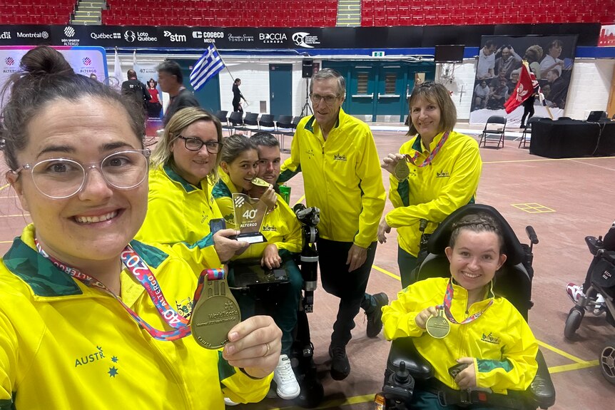 A group in yellow jumpsuits hold up medals.