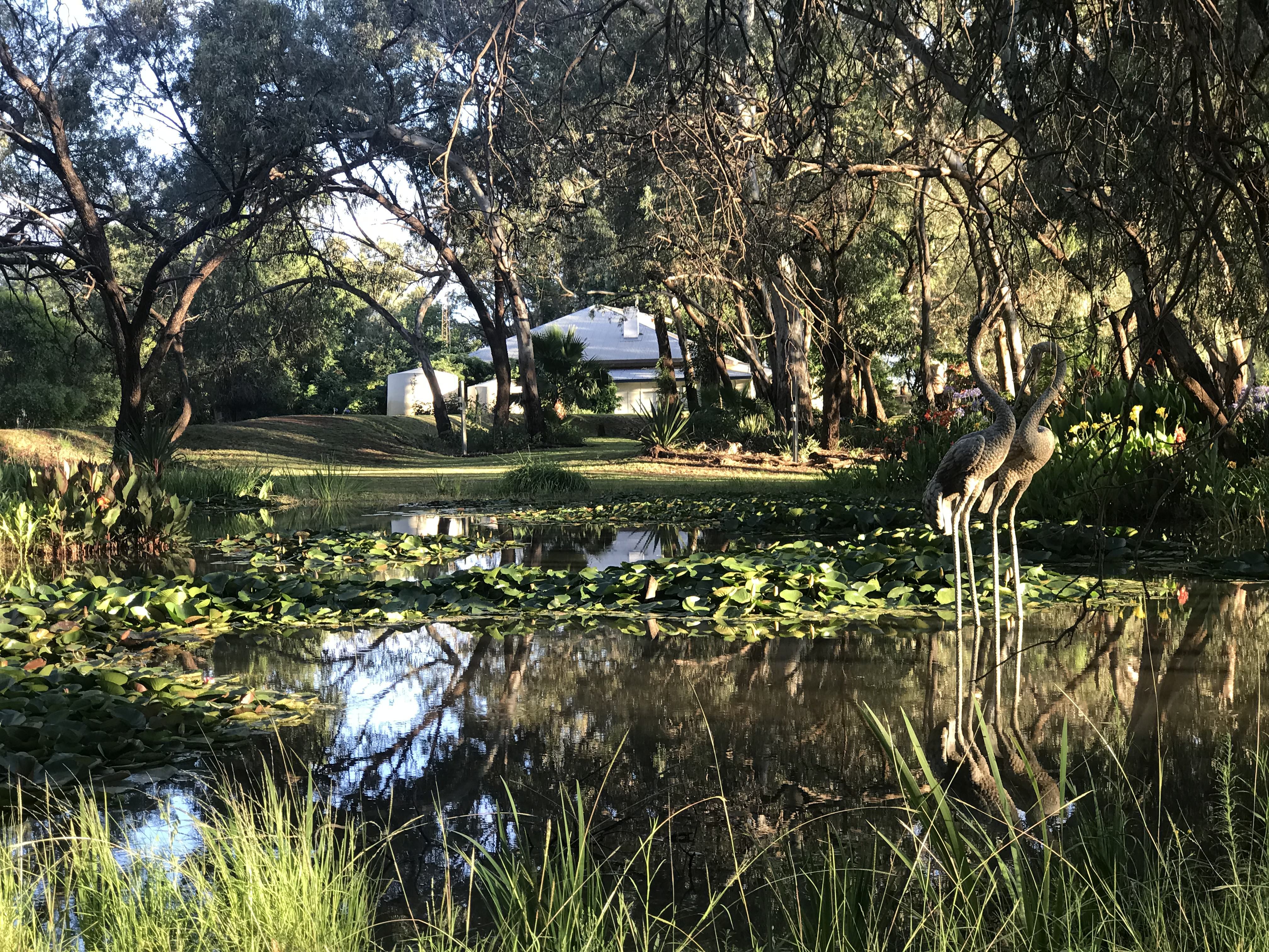 A view across a river to a single-level white house, surrounded by trees.