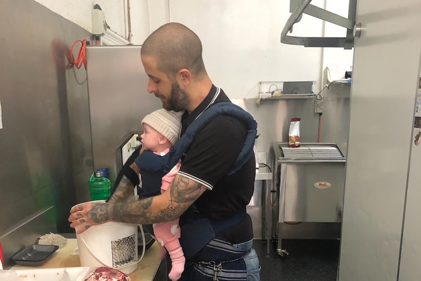 A man with a newborn baby harness making meat patties.