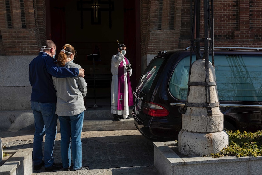 A priest wearing a face masks to protect against coronavirus performs funeral rites at a Madrid cemetery