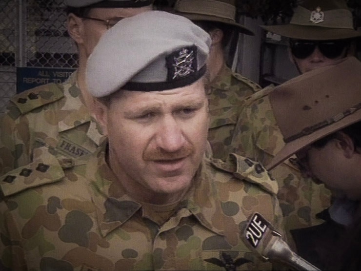 Man in a blue beret and army fatigues talking to media.