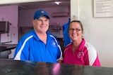 Butcher and his wife stand smiling behind counter of butchery. 