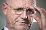 Tight headshot of David Leyonhjelm, from below. as he adjusts his glasses.