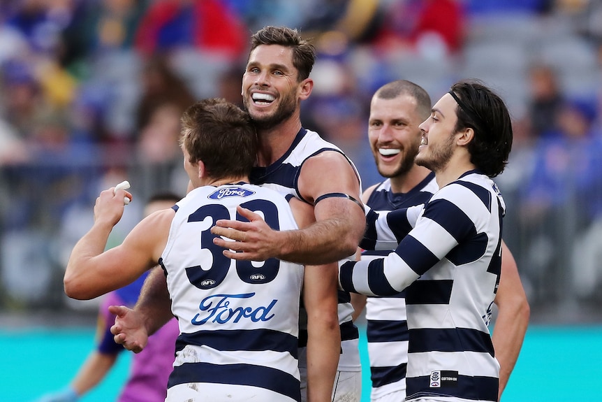 Tom Hawkins smiles widely as Geelong players surround and hug him