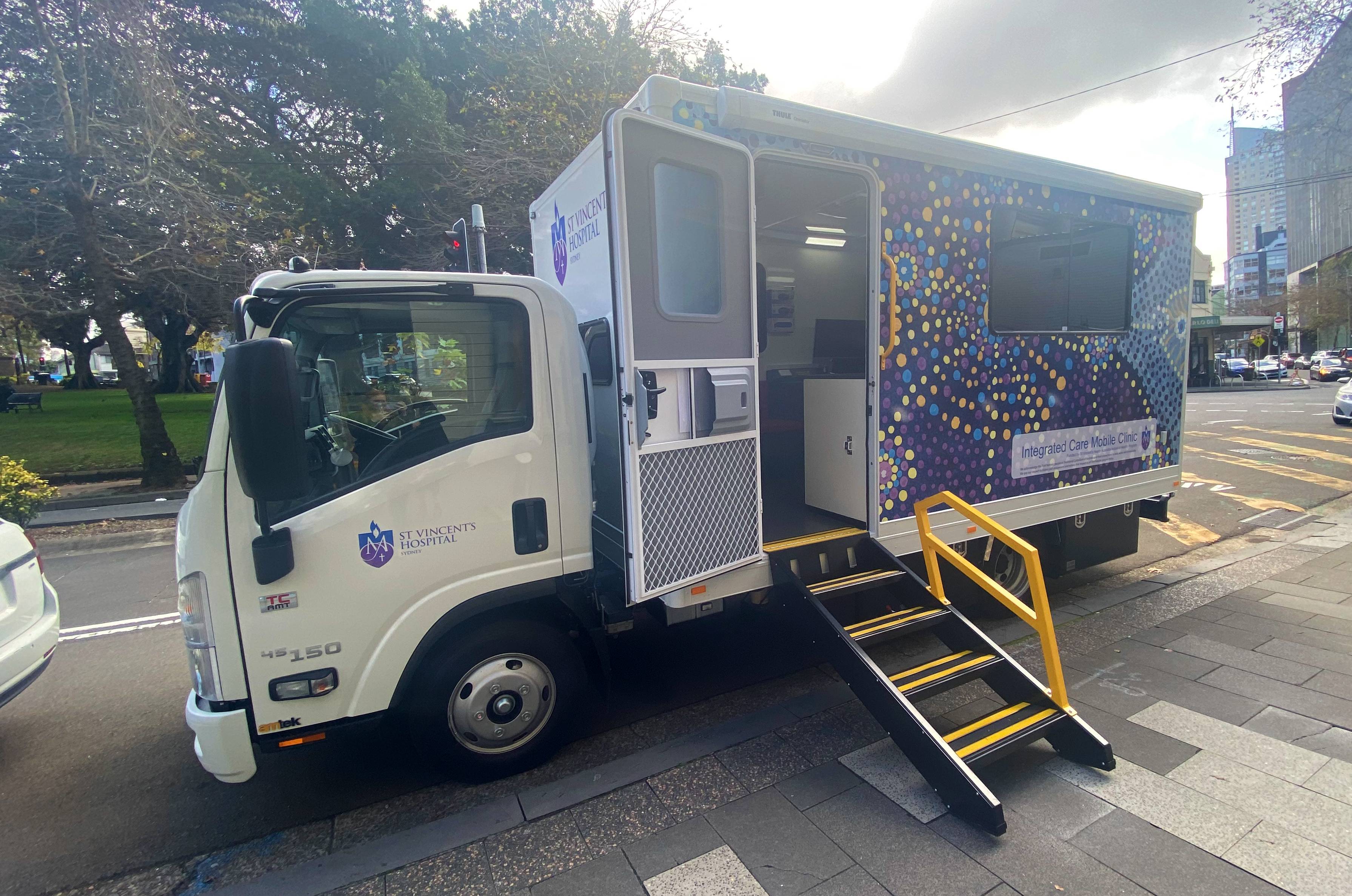 A truck that is brightly covered with a dot painting has a ramp leading to an open door