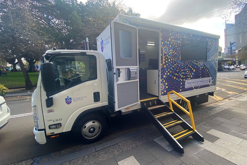 A truck that is brightly covered with a dot painting has a ramp leading to an open door
