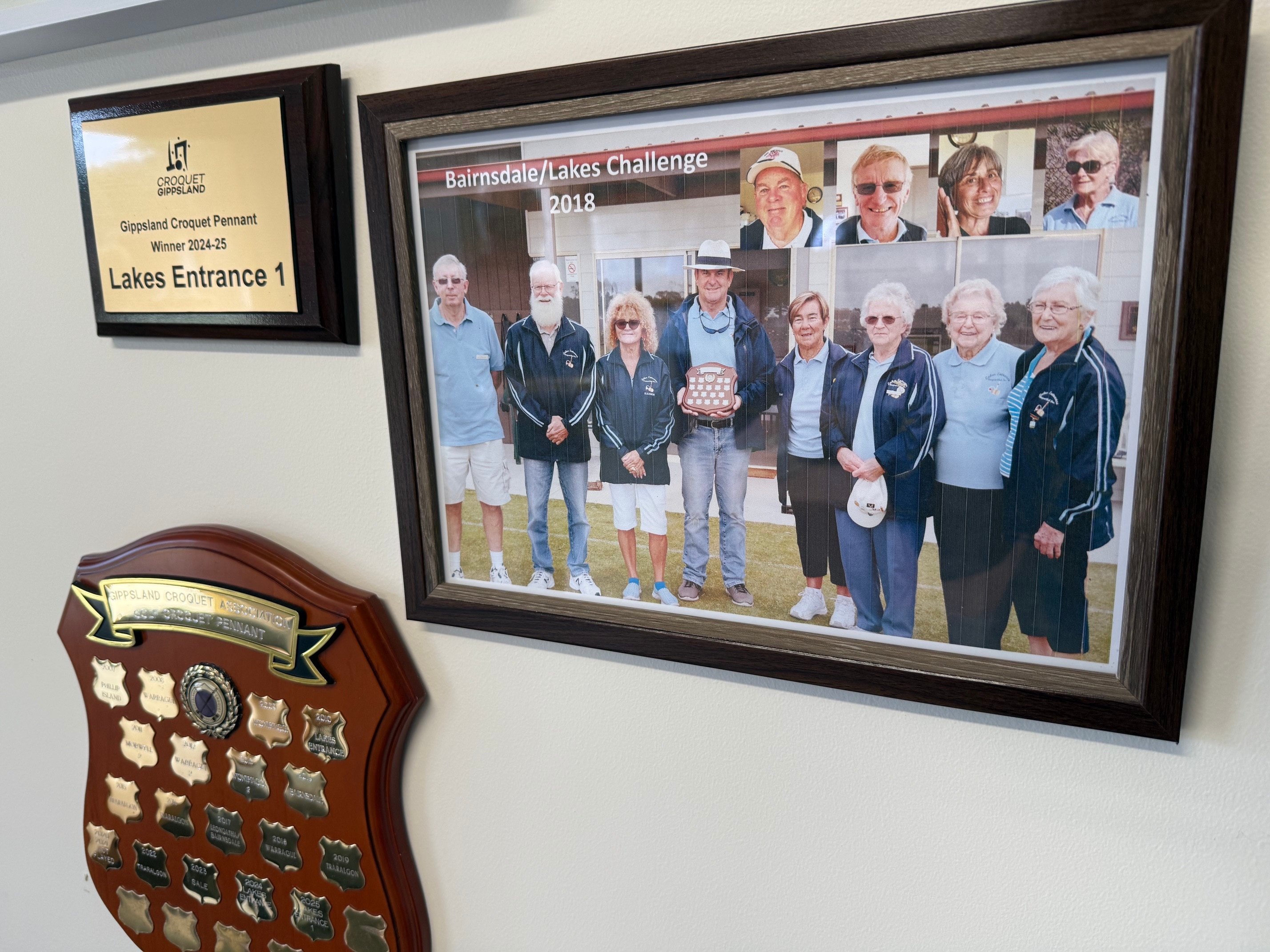 A photo showing croquet players, mounted on a wall next to trophies and plaques. 