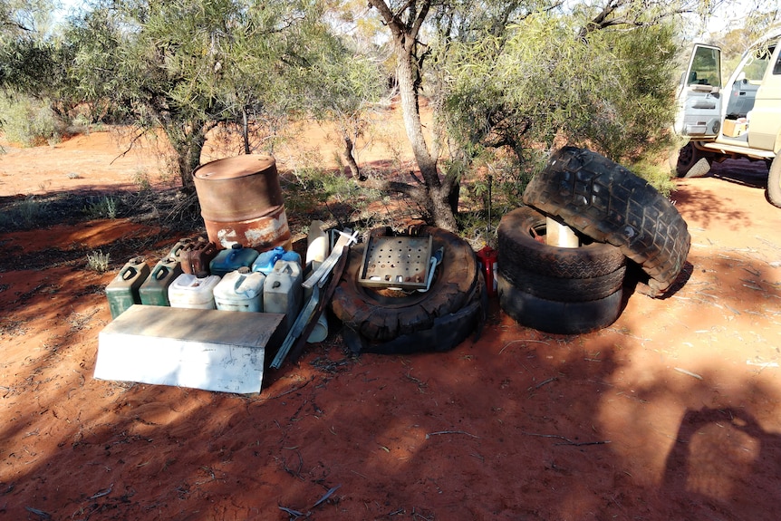 A collection of tyres and jerry cans under a tree next to a dirt road.