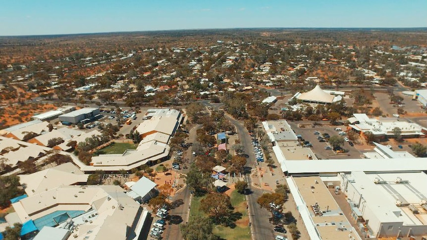 A wide main road with a green median strip opens up to a sprawling town in a desert.