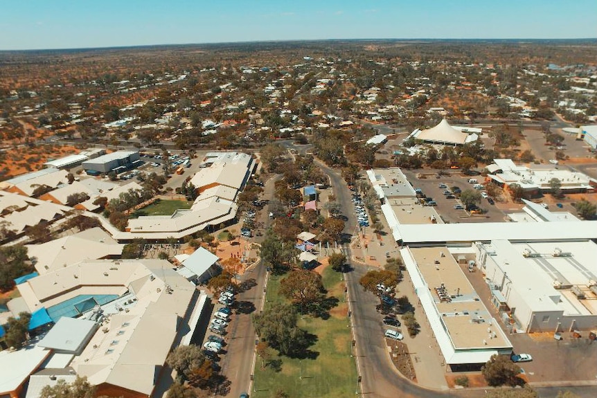 A wide main road with a green median strip opens up to a sprawling town in a desert.