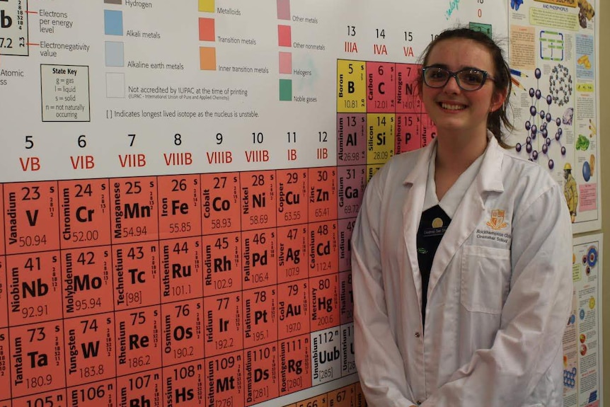 Courtney Smith in lab coat with large periodic table.