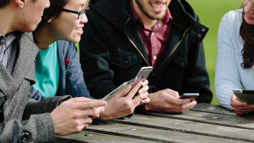 Young people sitting at an outdoor table using smart devices.