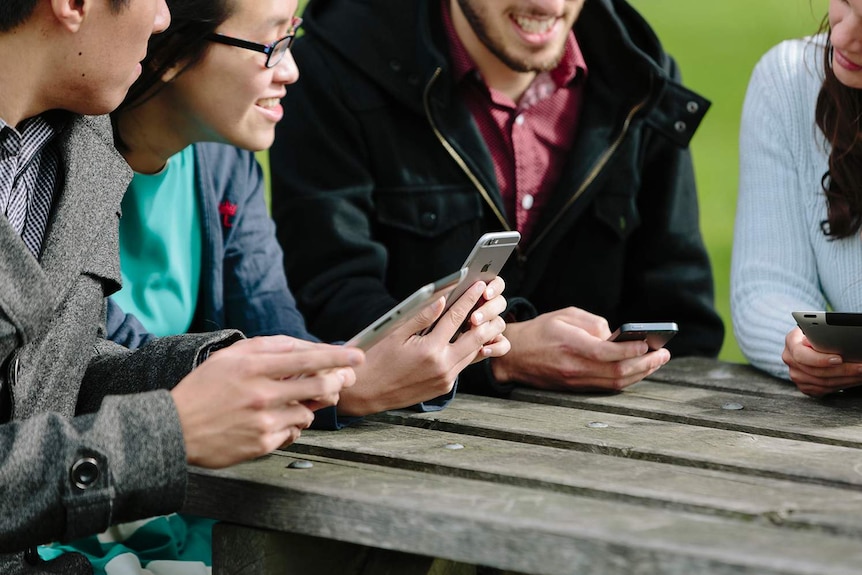 Young people sitting at an outdoor table using smart devices.