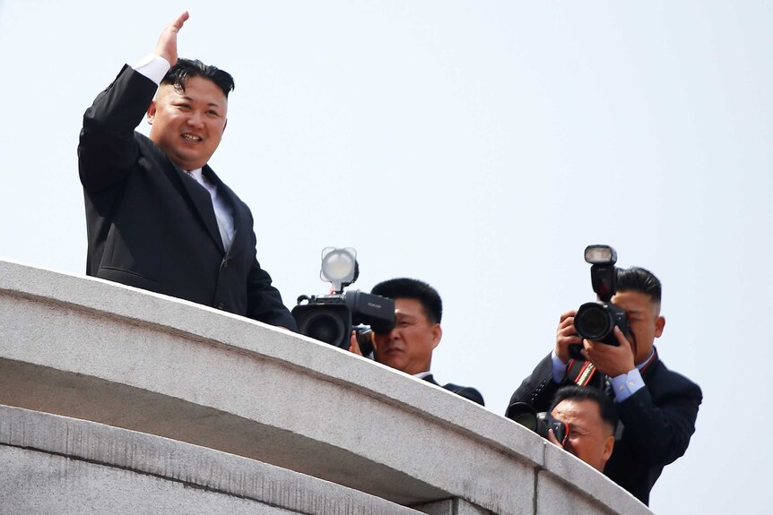 In Pyongyang North Korean leader Kim Jong Un waves to people attending a military parade.