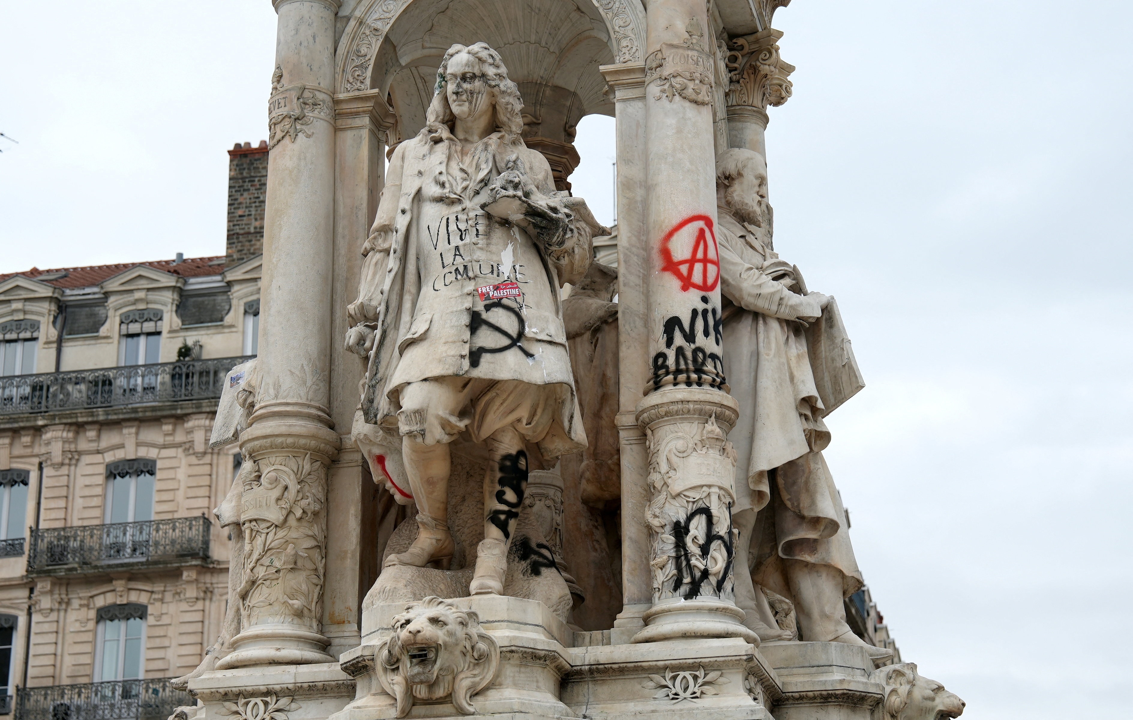 A large stone statue in a square covered in anarchist and communist graffiti.