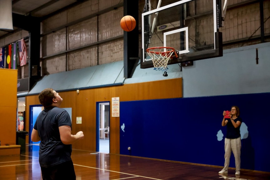 A young man shoots the basket and is watching as the ball heads towards the net.