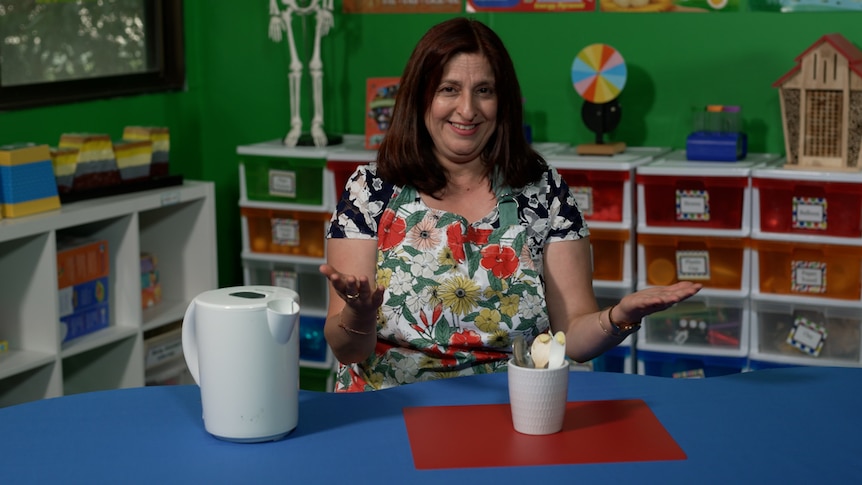 Female teacher in classroom with hands outstretched