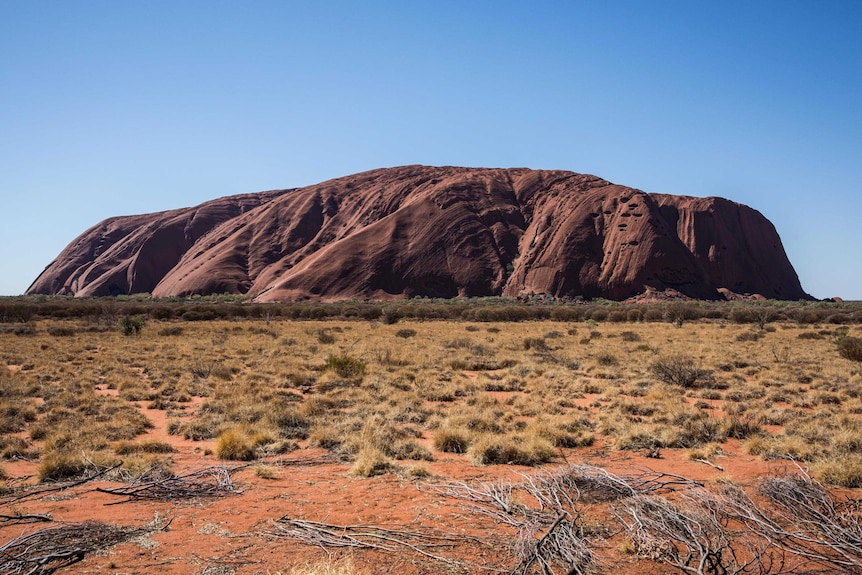 An image of Uluru, rock formation with the sun hitting its flank.