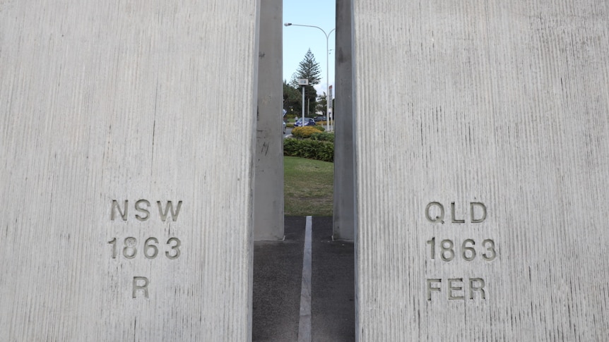 Two grey cement structures seperated by a white painted line, one side says QLD and the other NSW