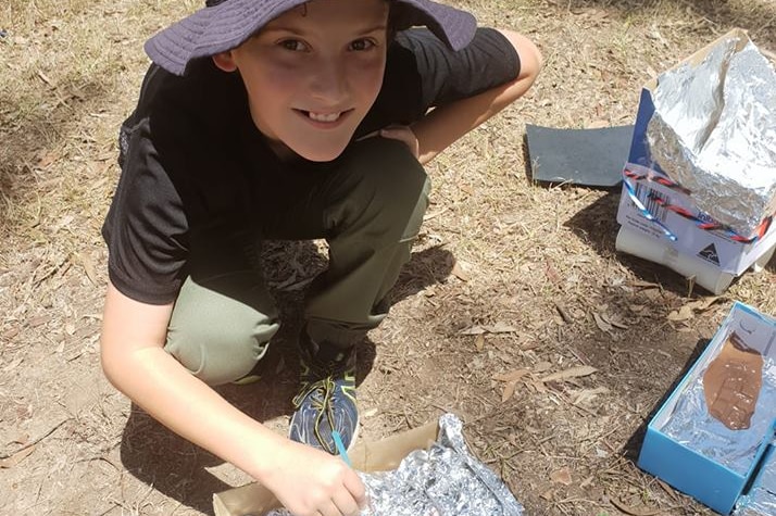 A school boy builds a solar oven with a box and tin foil.
