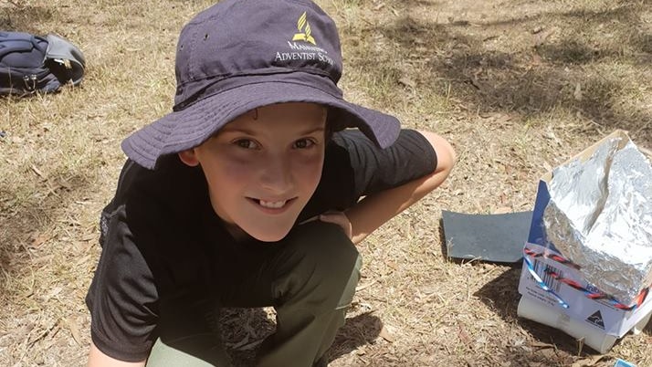 A school boy builds a solar oven with a box and tin foil.
